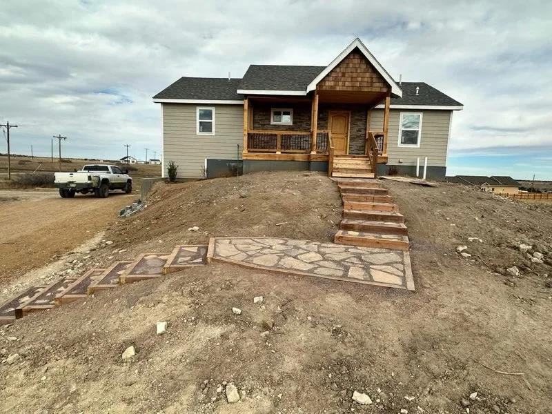 New home exterior with lap siding, stone veneer accents, wood porch, and flagstone walkway on a hillside lot