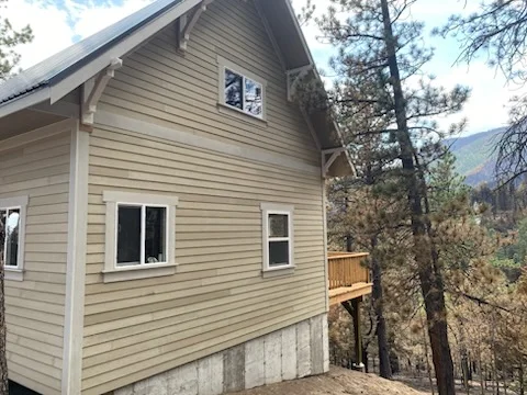 Tan horizontal lap siding and white-trimmed windows on a cabin with stone foundation and wood deck