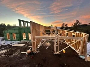 Residential wood framing construction with wall studs, window openings, and temporary bracing at dusk
