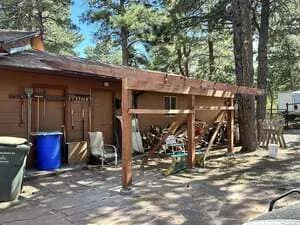 Wood-framed covered patio with open beam construction and attached storage shed in forest setting