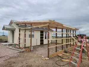 New residential addition under construction with covered porch, wooden framing, and metal railings