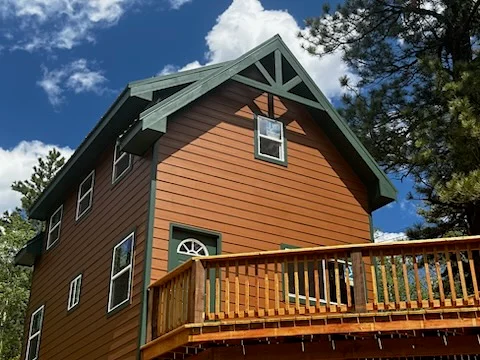 Two-story home with horizontal siding, green trim, and a raised wood deck with railing