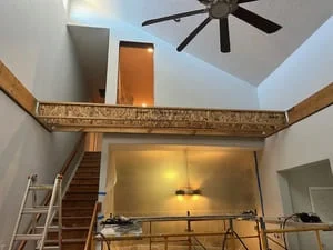Interior renovation with exposed wood beam, drywall, recessed lighting, and open staircase framing