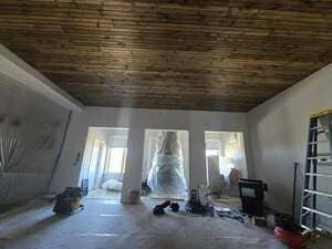 Interior room with dark wood plank ceiling, white drywall, and glass sliding doors during renovation